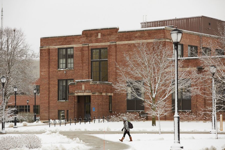 A wide shot of Morris Hall in the winter. A person is walking on the sidewalk in front of the building.
