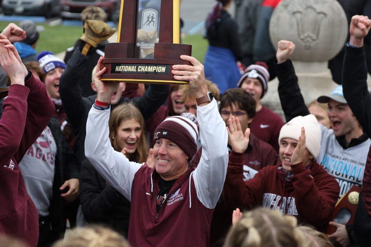 UWL Cross Country Head Coach Derek Stanley hoists the National Championship trophy surrounded by UWL runners at the NCAA Division 3 Cross Country National Championships in Terre Haute, Indiana. Image retrieved from Adam Weyer / @adams_t3.