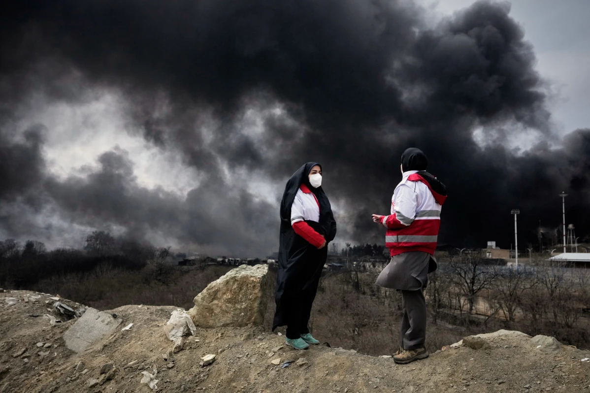 Crescent Society stand as a thick plume of smoke from a U.S.-Israeli strike on an oil storage facility late Saturday rises in the sky in Tehran, Iran, Sunday, March 8, 2026. Photo retrieved from AP Photo. Photographer: Vahid Salemi.